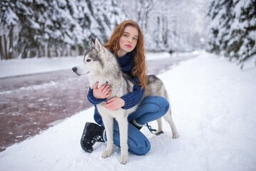 A red-haired girl crouching and hugging a husky dog on snow © Nomad_Soul
