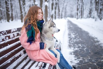 Red-haired girl holding a husky dog on a snowy park bench © Nomad_Soul