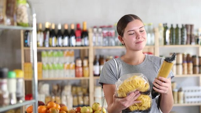 Youth girl choose and buy pasta in store. Market visitor consider and make choice of assortment, buy noodles. Client hesitates before buying, choose garnish product, reads package labels 