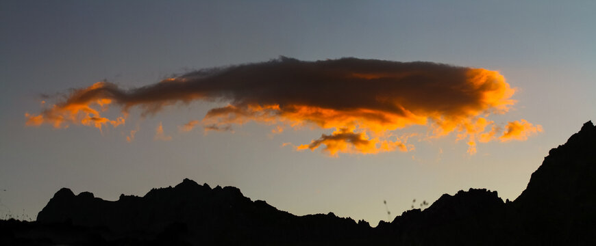 Golden hour cloud glows over silhouetted mountains