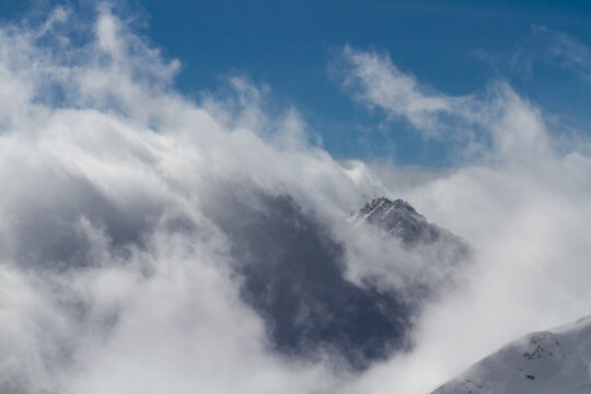Dramatic clouds swirling around a snowy mountain peak