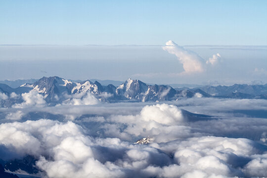 Snowy mountain range peaks poking through clouds