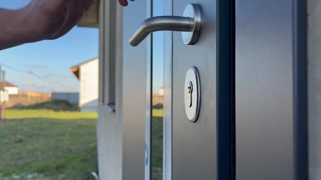 A male hand opens the new exterior entrance door of a country house to check the quality of its installation.