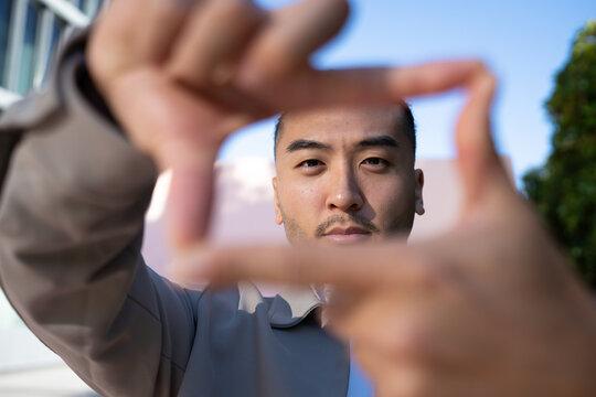 Man framing his face with hands outdoors under blue sky in Madrid
