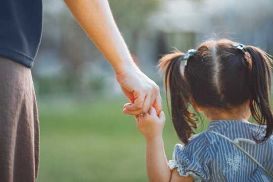 Close up rear view of mother gently holding little daughter hand while walking outdoors in green park, showing love, trust, protection and emotional connection, caring parenting, family bonding