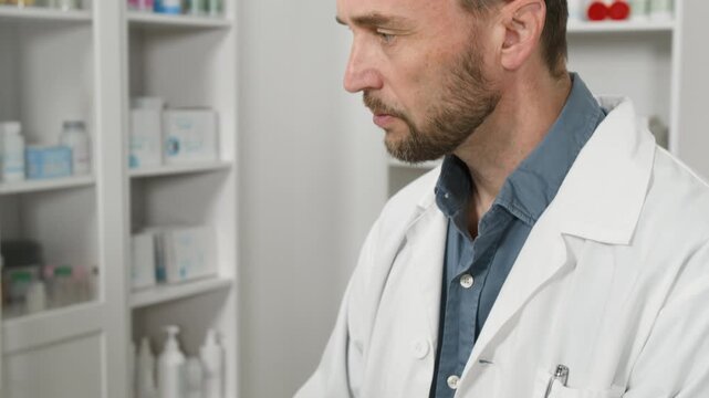 Middle aged Caucasian male pharmacist typing on computer keyboard in drugstore. Ideal for healthcare marketing, pharmaceutical software promotion, and medical training