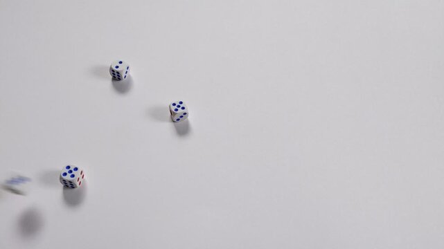 White dice with blue and red pips roll and scatter across a clean white surface in a minimalist tabletop scene