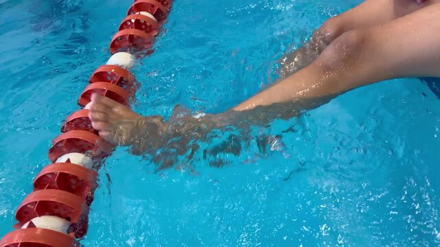 A person's legs kicking and splashing in the clear blue water of a swimming pool. Swimming lessons, aquatic sports, fitness training