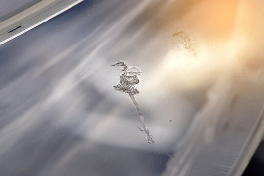 Deep scratch on plastic headlights lens cover, need for replacement. Car headlight lens with visible crack and chipped plastic, illuminated by bright sunlight, damaged headlight cover. Selective focus
