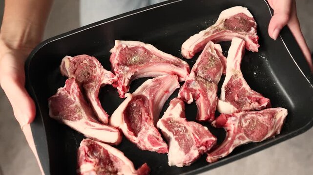 A single hand presents a full tray stacked high with fresh raw lamb cutlets
