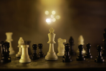 Dramatic Chess Board Focused on White King Surrounded by Pieces in Low Light © alexkich