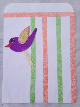 Purple glitter bird craft on white paper with orange and green tape stripes
