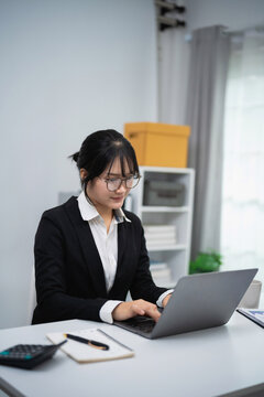 Young professional businesswoman working on laptop in modern office with notebook calculator and documents on desk