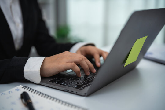 Businessperson working on laptop typing office desk close up with notebook pen and blurred background