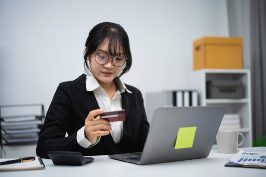 Professional young woman using credit card on laptop in modern office environment for online shopping payment