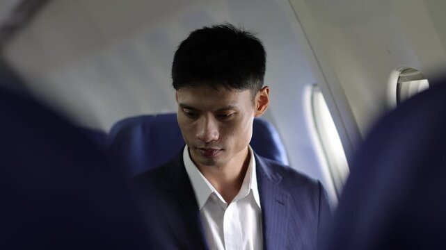 Asian businessman using a tablet during a flight. Asian businessman sitting in an airplane cabin and working on a digital tablet during a business trip. Man traveling by air.