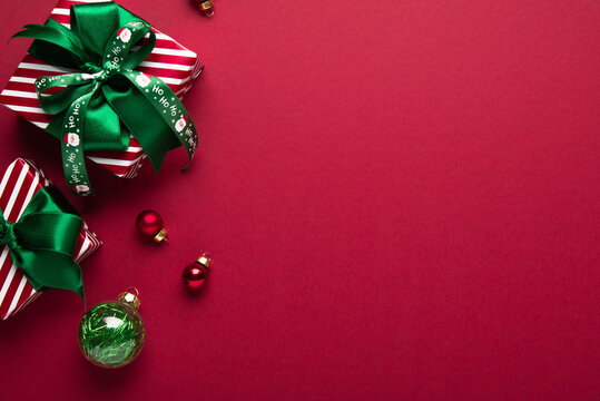 Red Christmas and Happy New Year holiday background with gift boxes, green ribbon bows and festive ornaments, flat lay with copy space. Greeting card.