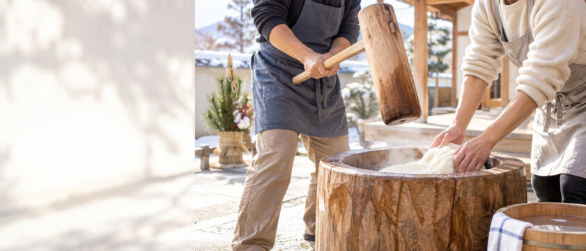 Japanese New Year mochi making, people pounding rice dough in traditional wooden usu and kine near sunlit home, festive cultural food preparation with generous copy space for seasonal banner design