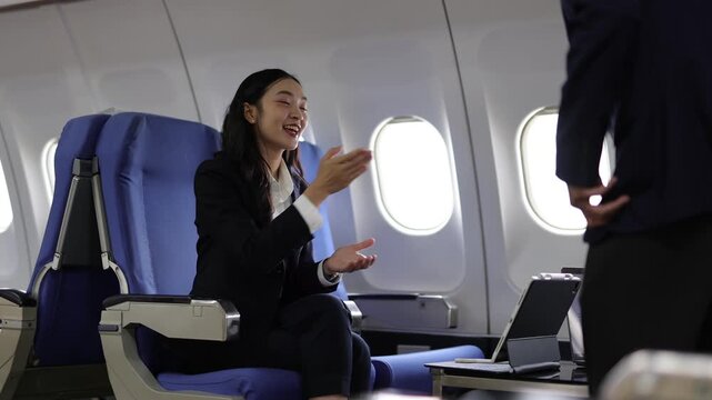 Businesswoman greeting a colleague on an airplane. Asian businesswoman in a suit sitting in business class, shaking hands and talking with a colleague during a flight for a work trip.