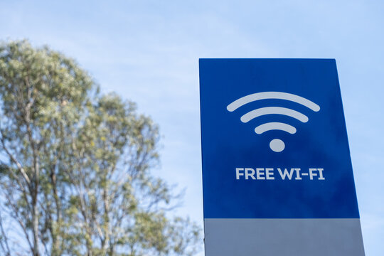 A blue signage post displaying a Wi-Fi icon and the text "FREE WI-FI"&nbsp;with blurred eucalyptus tree branches in the background. Public wireless internet&nbsp;access signage in Australia.
