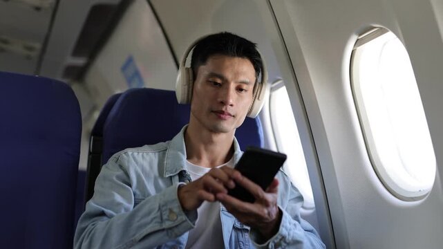 Young Asian man listening to music during airplane flight.