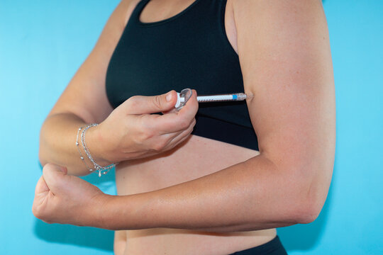 hand holding a syringe and injecting into the upper arm, muscular arm on a light blue background, anabolic steroids, hormones and peptides for muscle growth in sports and fitness, doping