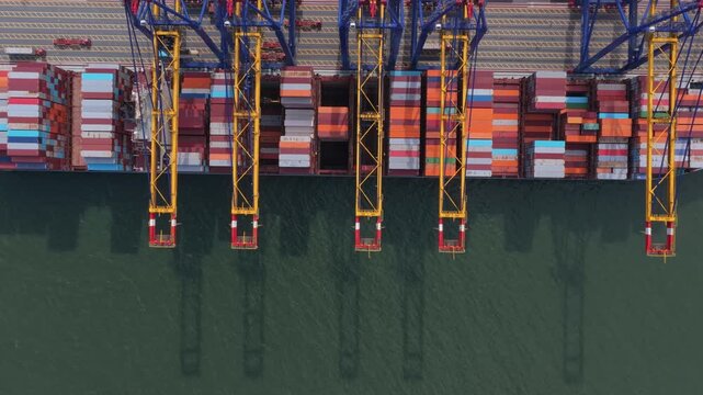 Top down aerial view of a large container ship being loaded with cargo by massive cranes at the industrial port of hai phong, vietnam