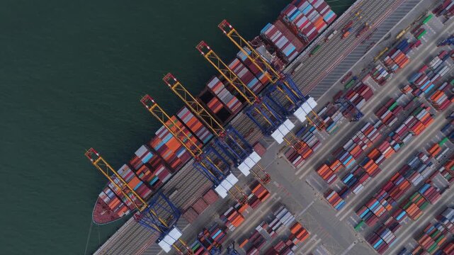 Top down aerial view of a large cargo vessel docking at the commercial port of hai phong, vietnam. Cranes are loading and unloading containers