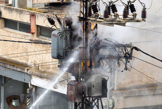 Close up view of water jet stream extinguishing burning high voltage power pole and electrical transformer emitting smoke and fire on city street