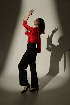Fashion Model Wearing a Bright Red Tie-Neck Blouse and Black Trousers, Elegant Smart Casual Style in Dramatic Studio Lighting with Strong Shadows and High Contrast