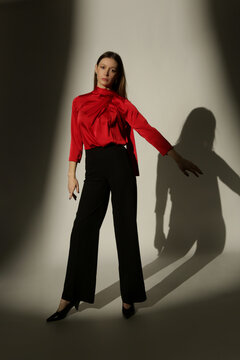 Fashion Model Wearing a Bright Red Tie-Neck Blouse and Black Trousers, Elegant Smart Casual Style in Dramatic Studio Lighting with Strong Shadows and High Contrast