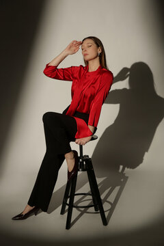 Fashion Model Wearing a Bright Red Tie-Neck Blouse and Black Trousers, Elegant Smart Casual Style in Dramatic Studio Lighting with Strong Shadows and High Contrast
