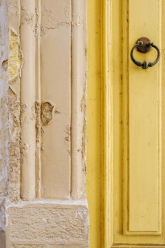 Yellow wooden door with antique metal knocker and weathered stone wall