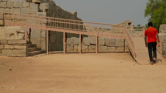 traveler walking along an elevated access ramp towards ancient granite ruins and carved stone structures on Royal Enclosure at hampi, vijayanagara empire, karnataka, india. day time, static shot, 4k.