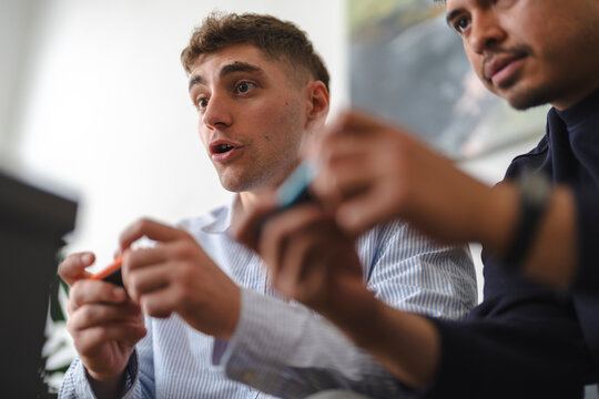 Two young male friends sit together on a comfortable couch, holding video game controllers and playing an intense multiplayer game with deeply focused expressions.