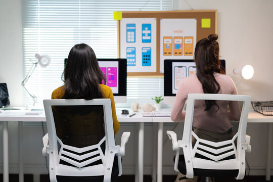 Female web developer creating UX UI wireframe layouts for smartphone apps on a computer in a modern office workplace.