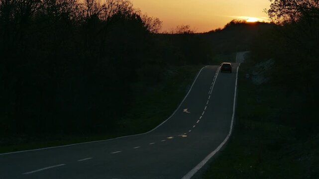 Tilt shift miniature effect of a steep rolling asphalt road through the forest, cars driving on a bumpy straight highway with vertical hills and dips at sunset outdoors in countryside