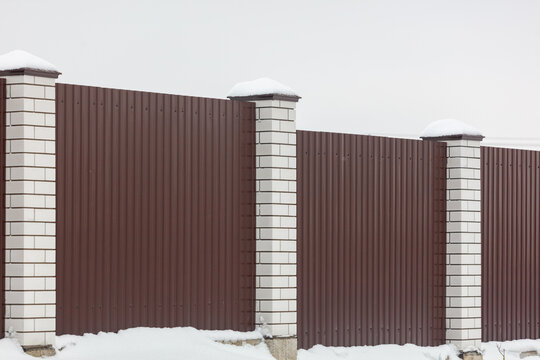 Snow rests atop brown metal fence pillars