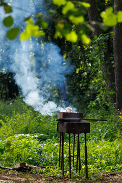 Smoke rises from a wooden grill in a green forest