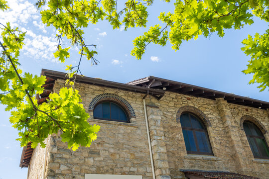 Exterior wall of historic Bridgewater Hall in the Adelaide Hills, South Australia, with rustic stone masonry wall&nbsp;framed overhead by green oak tree branches. Australian regional heritage preservation.
