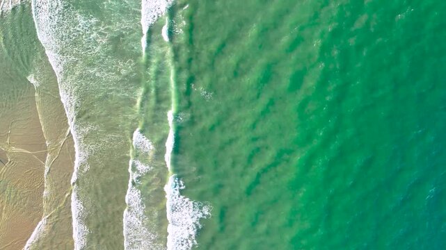 From above, turquoise water rolls in gentle white waves over a sandy beach on the Da Nang coast, where sea and shore meet in soft patterns