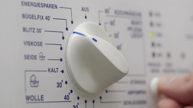 Close-up of a person's hand pouring detergent and turning on a washing machine, selecting a program mode and pressing the "Start" button on the control panel.