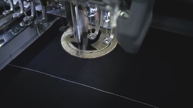 Closeup of industrial embroidery machine stitching circular logo on black fabric