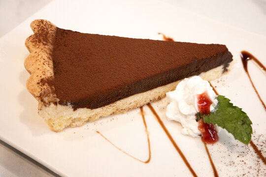 Slice of rich dark chocolate tart dessert served on white plate