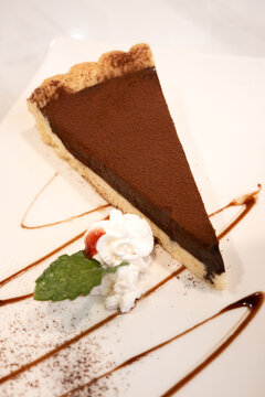 Slice of rich dark chocolate tart dessert served on white plate