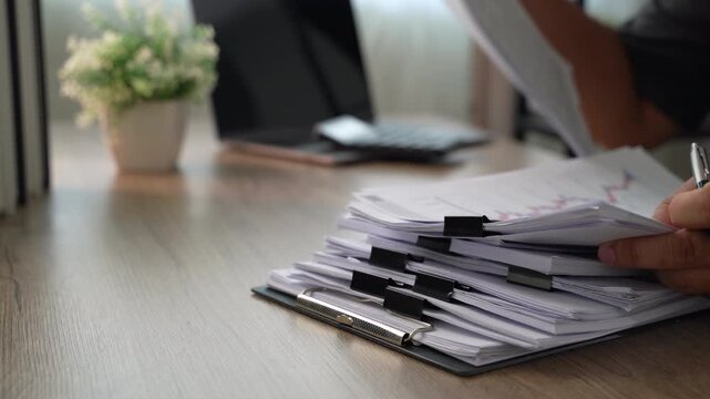 Business professional calculating figures across financial statements and accounting paperwork, using calculator and pen for tax planning, deductible expenses and tax preparation work.