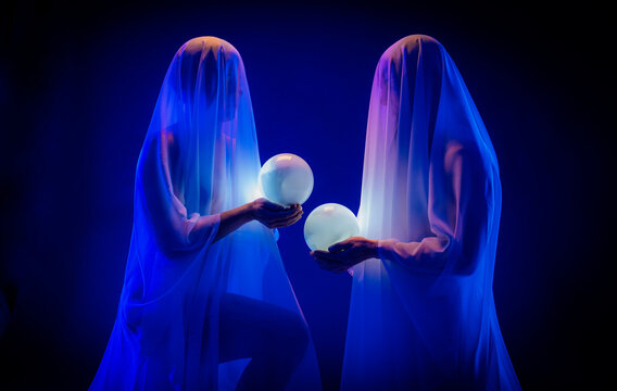 Ghostly figures holding glowing crystal balls in dark light