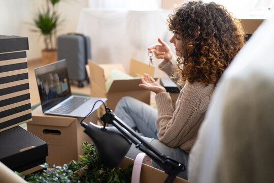White woman holding keys during video call surrounded by moving boxes