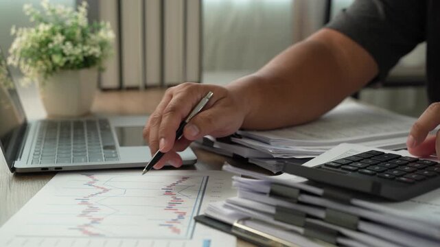 Professional sorting accounting documents and checking calculations with calculator and pen beside laptop, reviewing budget records, business expenses and financial paperwork for analysis.