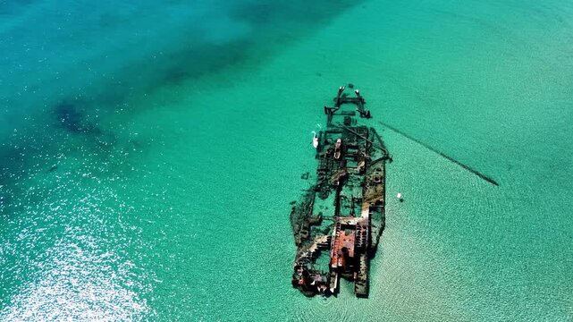 Slow aerial tracking shot of gentle ocean waves splashing against corroded steel hull of grounded shipwreck